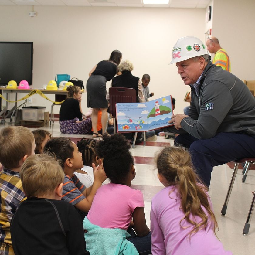 person in hard hat reading a book to children