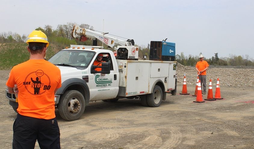 two people in safety gear standing next to a work truck and cones